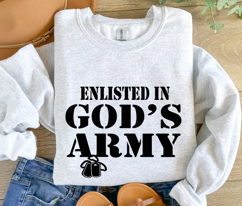 May include: A gray sweatshirt with the text "Enlisted in God's Army" in black lettering. The text is in a bold, blocky font. There are two small black dog tags hanging below the text.