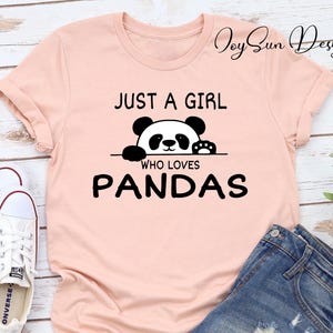 May include: A pink t-shirt with the text "Just a girl who loves pandas" and a black and white panda peeking over the top.