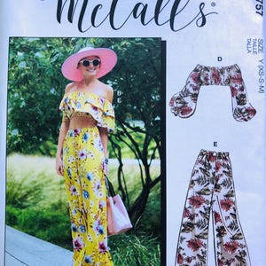 Puede incluir: Patrón de costura McCall's M7757. La imagen muestra a una mujer con un conjunto floral amarillo, que incluye un top corto y pantalones de pierna ancha. Otro diseño muestra un top y pantalones similares con un estampado floral diferente. El texto "#CharlotteMcCalls" es visible.