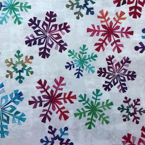 May include: A white fabric with a repeating pattern of colorful snowflakes. The snowflakes are in shades of blue, green, red, and purple.