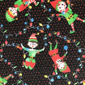 May include: A black fabric with a repeating pattern of Christmas elves and string lights. The elves are wearing green and red outfits with matching hats. The string lights have colorful bulbs.