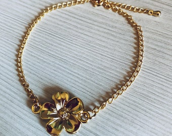 May include: A gold chain bracelet with a gold flower charm. The bracelet has a lobster clasp closure.