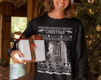 May include: Black Christmas sweater with a festive design. The sweater features the text "CHRISTMAS PARTY 1988" with images of guns and cars. The sweater also has the text "HO-HO-HO" and "YIPPEE-HI-YAY!" The person in the image is wearing a Santa hat.