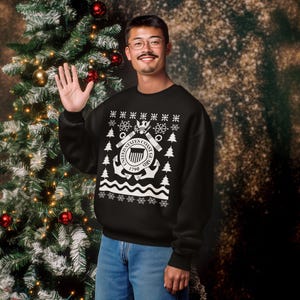 May include: Black sweatshirt with a white graphic of the United States Coast Guard emblem, snowflakes, and Christmas trees. The sweatshirt is worn by a person standing next to a decorated Christmas tree.