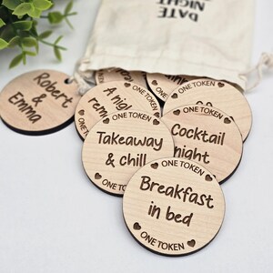 May include: Wooden tokens with different date night ideas written on them, including "Cocktail night", "Breakfast in bed", and "Takeaway & chill". The tokens are in a small white drawstring bag with the words "Date Night Tokens" printed on it.