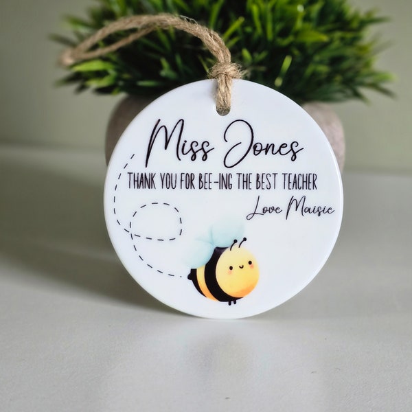 May include: White ceramic ornament with a bee design and the text "Miss Jones, Thank you for bee-ing the best teacher, Love Maisie".