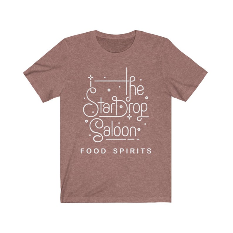 May include: A short-sleeved, mauve t-shirt with the white text "The StarDrop Saloon" and the words "FOOD SPIRITS" below. The design features stylized lettering and decorative elements.