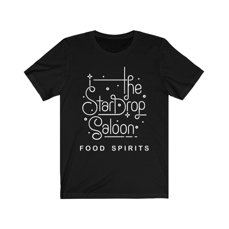 May include: Black t-shirt with a white graphic that reads "The StarDrop Saloon" in a stylized font. Below the saloon name, the text "FOOD SPIRITS" is printed in a clean, sans-serif font. The shirt is made of a soft material.