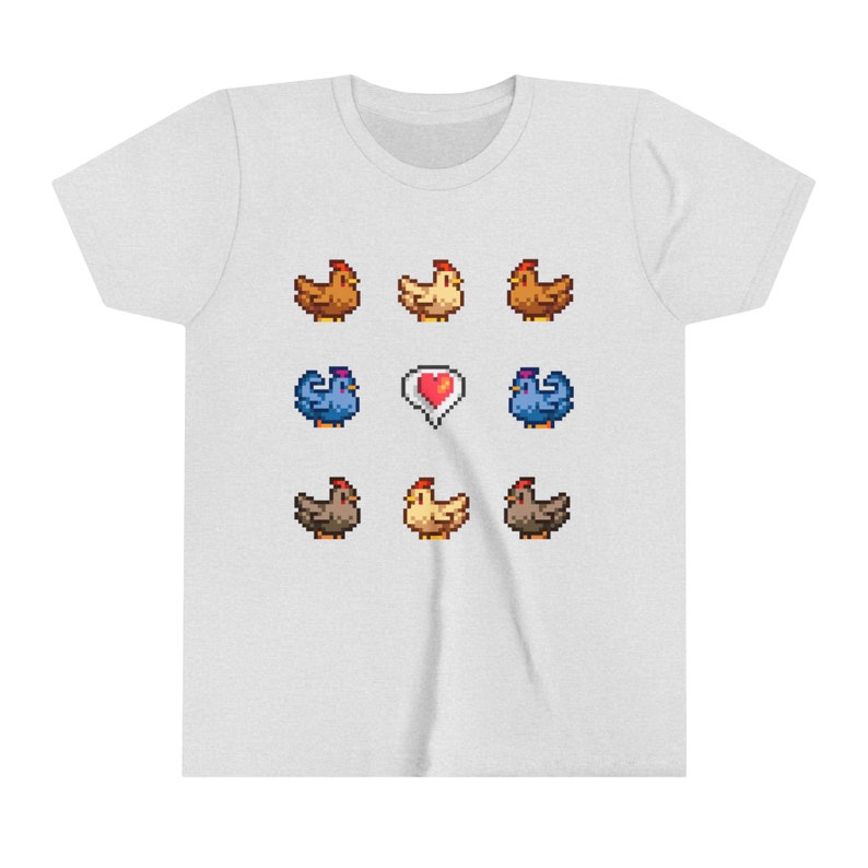 Pu&ograve; includere: Una maglietta bianca con un design a pixel di galline e un cuore. Le galline sono marroni, gialle e blu.