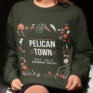 May include: A dark green sweatshirt with a white graphic design featuring the text "Pelican Town - Est. 2016 Stardew Valley" surrounded by various farm-themed icons.