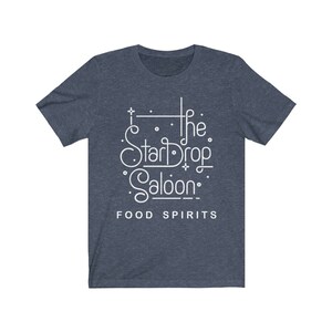 May include: A navy blue t-shirt with white text that reads "The StarDrop Saloon" in a stylized font. Below the name, the words "FOOD SPIRITS" are printed in a smaller font. The shirt has short sleeves and a crew neck.