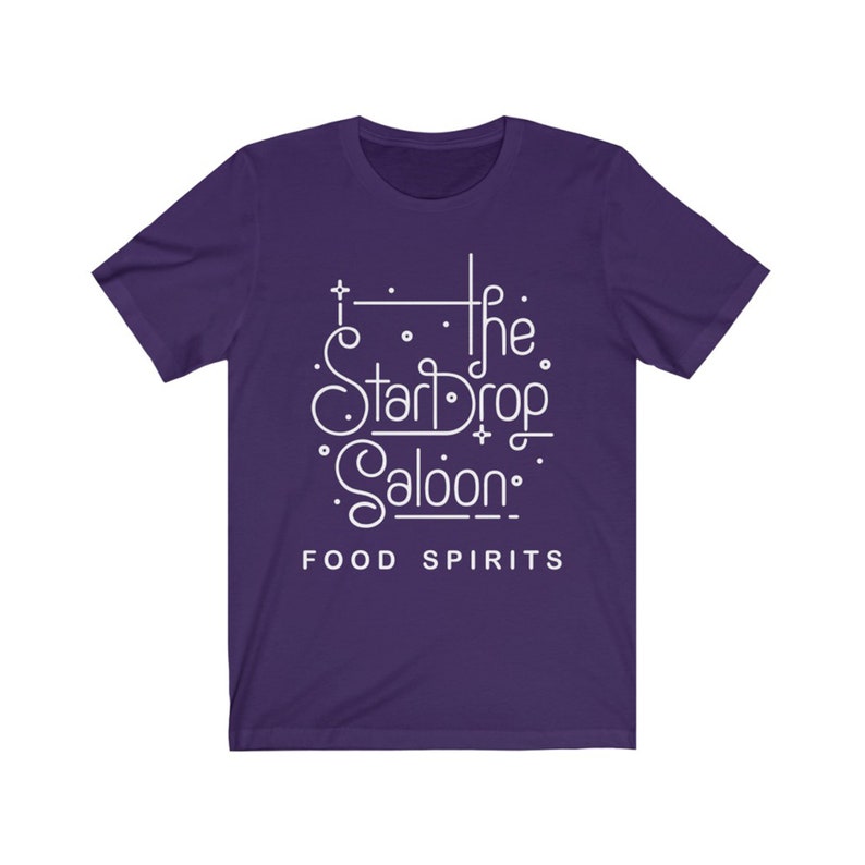 May include: A purple t-shirt with the white text "The StarDrop Saloon" in a stylized font. Below the name are the words "FOOD SPIRITS" in a simple sans-serif font. The shirt has short sleeves and a crew neck.