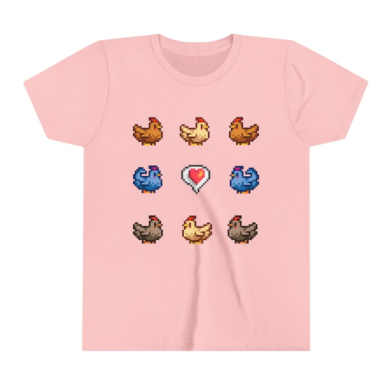 Pu&ograve; includere: Una maglietta rosa con un design a pixel di galline e un cuore. Le galline sono marroni, gialle e blu.