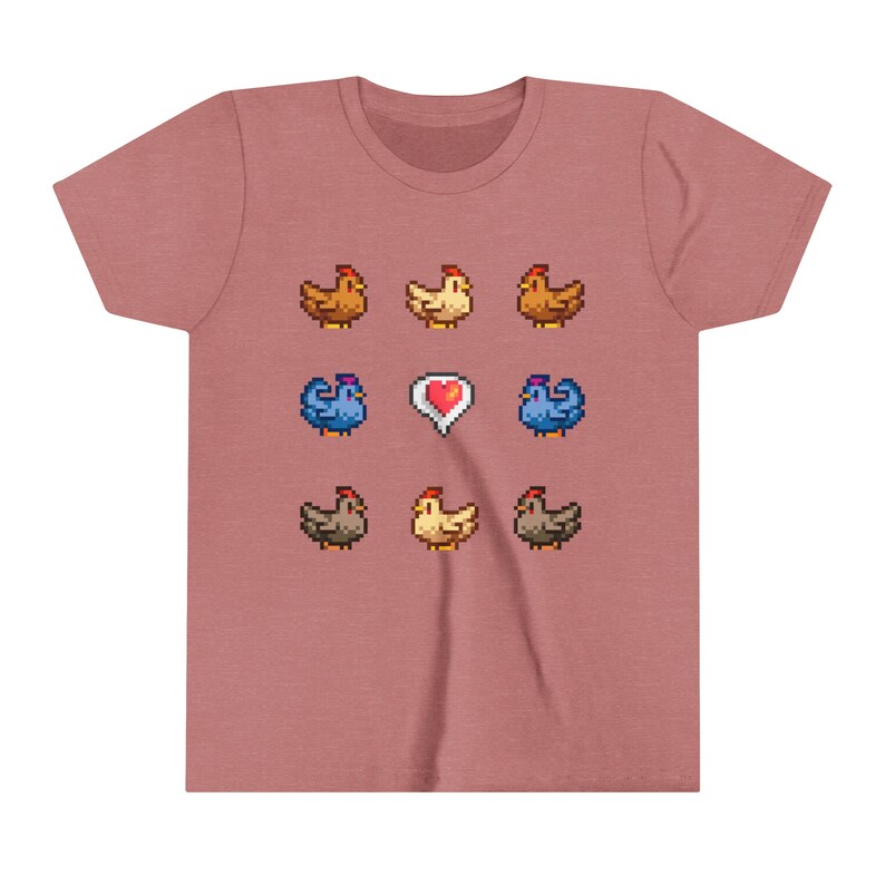 Pu&ograve; includere: Una maglietta rosa con un design a pixel di nove galline e un cuore. Le galline sono marroni, gialle e blu.