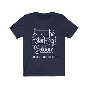 May include: Navy blue t-shirt with the white text "The StarDrop Saloon" in a decorative font, with the words "FOOD SPIRITS" below. The shirt has short sleeves and a crew neck.