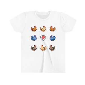 Pu&ograve; includere: Maglietta bianca con un design a pixel di nove galline e un cuore rosso. Le galline sono marroni, bianche e blu.