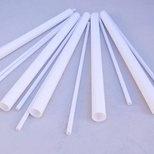 Könnte beinhalten: Eine Sammlung weißer Kunststoffstäbe in verschiedenen Längen und Durchmessern. Die Stäbe sind fächerförmig auf einer hellgrauen Oberfläche angeordnet.