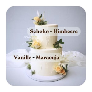 May include: A two-tiered wedding cake decorated with white buttercream frosting and fresh flowers. The top tier is labeled "Schoko - Himbeere" and the bottom tier is labeled "Vanille - Maracuja".