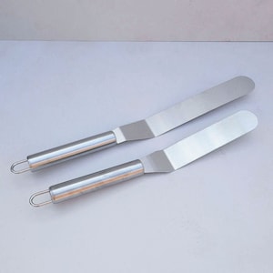 Könnte beinhalten: Zwei silberne Offset-Spatel aus Metall mit abgerundeten Kanten und einem Schlaufe-Griff.