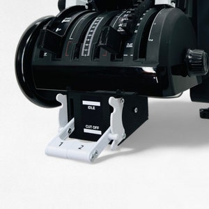 Op de afbeelding: Een zwart-wit vliegtuigbedieningspaneel met meerdere schakelaars en knoppen. Het paneel heeft een zwarte basis met een witte hendel en een witte knop. Het paneel is gelabeld "FLAPS" en heeft een kleine witte schakelaar met de tekst "CUT OFF" en "IDLE".