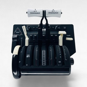 May include: A black aircraft control panel with multiple knobs, switches, and levers. The panel has a white label that reads "A/T DISENGAGE".