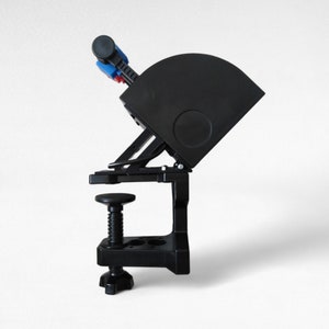 May include: A black clamp-on phone holder with a swivel arm and a blue and red button. The holder is designed to attach to a desk or table.