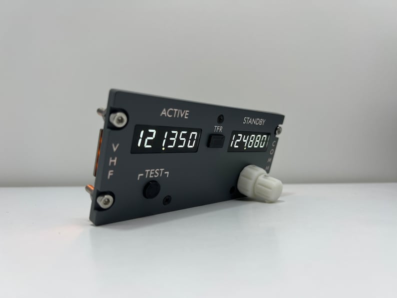 May include: A black and gray aircraft radio transceiver with a digital display showing "12.1350" and "124.880". The transceiver has a knob and buttons labeled "ACTIVE", "STANDBY", "TFR", "TEST", "VHF", "HF", and "COM".
