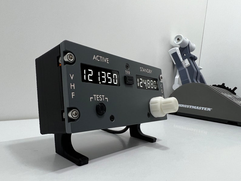 May include: A gray and black radio transceiver with a digital display showing "121.350" and "124.880". The transceiver has a knob on the right side and a "TEST" button on the front.