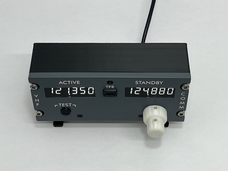 May include: A gray and black radio transceiver with a digital display showing "121350" and "124880". The transceiver has a "TEST" button, a "TFR" button, and a knob on the right side. The transceiver is labeled "ACTIVE" and "STANDBY".