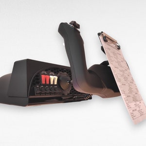 May include: Black flight simulator control panel with a variety of buttons and switches. A black joystick is attached to the panel and a clipboard with a checklist is attached to the joystick.