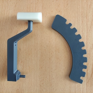 May include: A gray plastic gear with a white plastic handle. The gear has a series of teeth around the edge. The handle is attached to a gray plastic base.