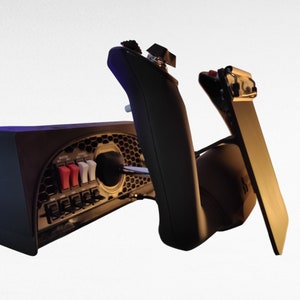 May include: A black gaming controller with a variety of buttons and switches. The controller is connected to a black base with a honeycomb pattern. The base has a red and white switch and a black lever.