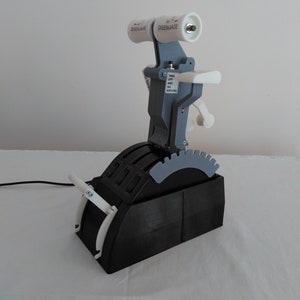 以下が含まれることがあります： 黒、グレー、白のフライトシミュレーターのスロットルクアドラント。デバイスには複数のレバー、ボタン、および「DISENGAGE」とラベル付けされたハンドルがあります。「TAKE OFF AND GO AROUND」というテキストも表示されます。黒いケーブルがベースから伸びています。