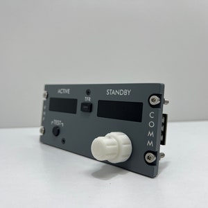 May include: Gray aircraft communication panel with a white knob, labeled "ACTIVE", "STANDBY", "TFR", "TEST", and "COMM".