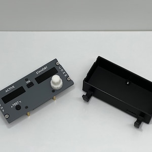 May include: A gray and black electronic device with a knob and two digital displays labeled "ACTIVE" and "STANDBY". The device is in a black plastic case.