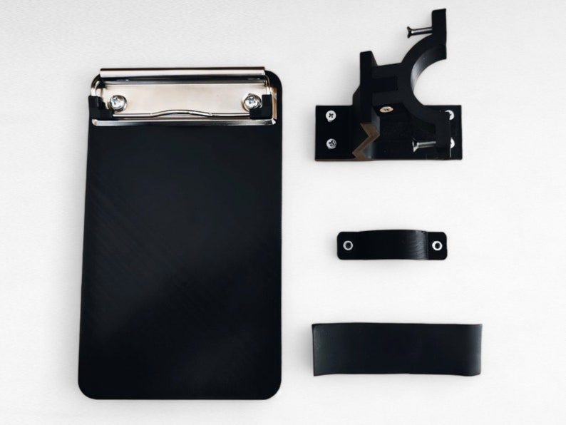 May include: A black clipboard with a silver clip and a black plastic mounting bracket, a black plastic handle, and a black plastic strap.