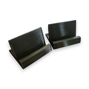 Könnte beinhalten: Zwei schwarze, 3D-gedruckte Telefonständer. Jeder Ständer hat eine rechteckige Basis und eine Rückenstütze, um ein Telefon aufrecht zu halten. Die Ständer bestehen aus einem strukturierten Material.