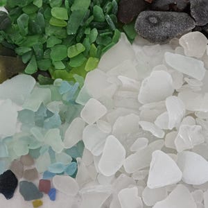 May include: A collection of sea glass in various colors, including green, white, blue, and brown. The pieces are irregular in shape and size, with a frosted appearance. The sea glass is arranged in a close-up shot.