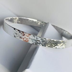 May include: A silver hammered bangle bracelet. The bracelet is smooth and shiny, with a hammered texture.