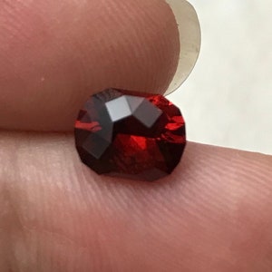 Puede incluir: Una piedra preciosa de color rojo intenso con un corte rectangular, sostenida en una mano.