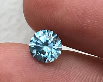 Può includere: Una pietra preziosa rotonda di colore blu chiaro con taglio a faccette.