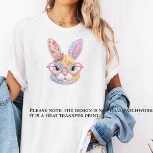 Peut inclure: T-shirt blanc avec un visage de lapin coloré portant des lunettes en forme de cœur. Le lapin a des oreilles à motifs floraux et un motif patchwork. Le texte au bas du t-shirt se lit comme suit : "PLEASE NOTE: THE DESIGN IS NOT REAL PATCHWORK: IT IS A HEAT TRANSFER PRINT."