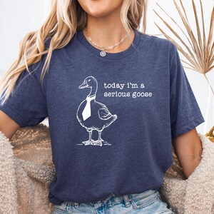 Pu&ograve; includere: Una maglietta blu navy con una grafica bianca di un'oca che indossa una cravatta. Il testo "today i'm a serious goose" &egrave; stampato sulla maglietta.
