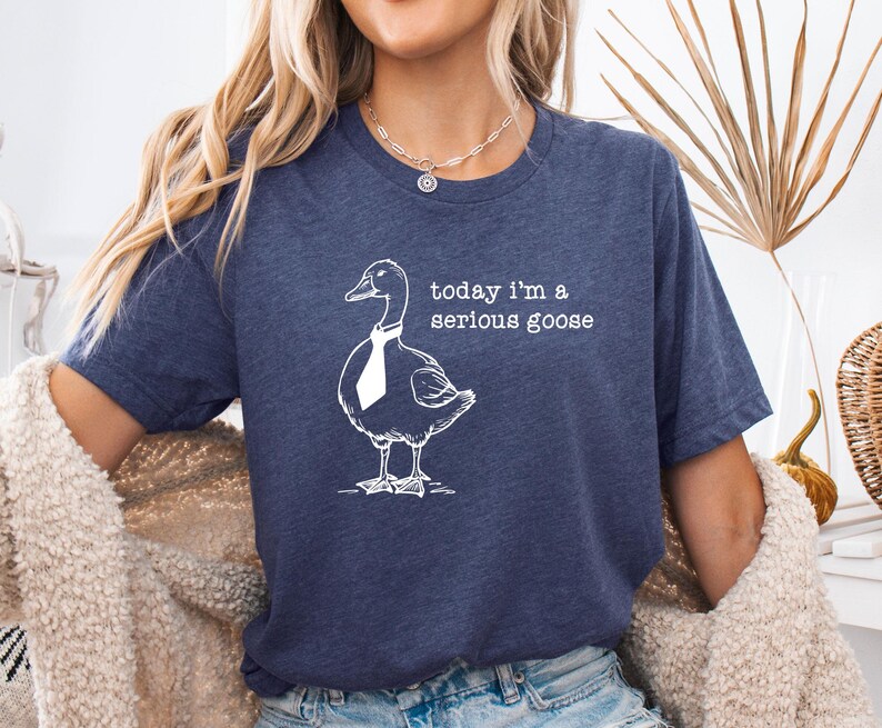 Pu&ograve; includere: Una maglietta blu navy con una grafica bianca di un'oca che indossa una cravatta. Il testo "today i'm a serious goose" &egrave; stampato sulla maglietta.