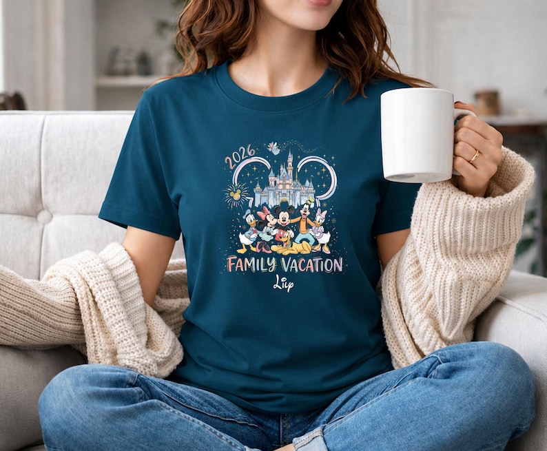 May include: A teal t-shirt featuring a graphic of Disney characters, a castle, and the text "2026 Family Vacation". The design includes Mickey Mouse, Minnie Mouse, Donald Duck, Daisy Duck, and Goofy. The shirt is a crew neck and has short sleeves.