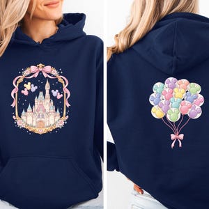 May include: Navy blue hoodie featuring a castle design on the front, framed by a pink bow and floral elements. The back of the hoodie displays a cluster of colorful paw print balloons tied with a pink bow. The hoodie has a front pocket and a hood.