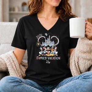 May include: Black V-neck t-shirt featuring a colorful graphic of Disney characters in front of a castle, with the text "2026 Family Vacation". The shirt is a comfortable, casual style.
