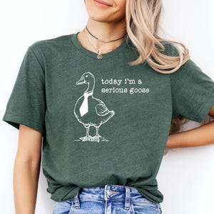 Pu&ograve; includere: Una maglietta verde con un'illustrazione bianca di un'oca con una cravatta e il testo "today i'm a serious goose".