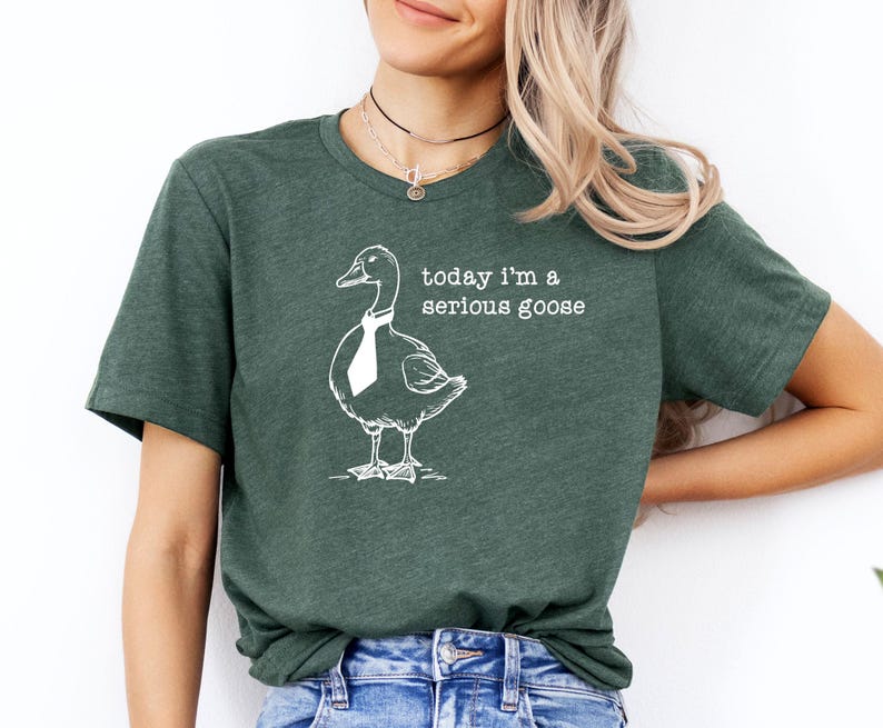 Pu&ograve; includere: Una maglietta verde con un'illustrazione bianca di un'oca con una cravatta e il testo "today i'm a serious goose".