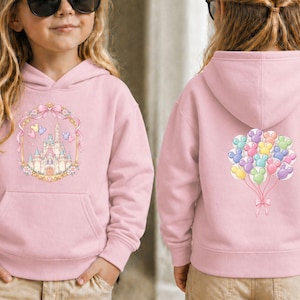 May include: A light pink hooded sweatshirt featuring a front graphic of a castle within a decorative frame, and a back graphic of colorful mouse-shaped balloons. The sweatshirt has a front pocket and a hood.